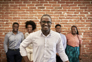 Lächelnder Geschäftsmann mit männlichen und weiblichen Kollegen, die im Hintergrund in einem Coworking-Büro stehen - ZEDF04208
