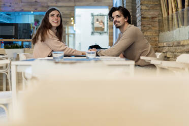 Junges Paar, das in einem Restaurant sitzt und wegschaut - EGAF02332