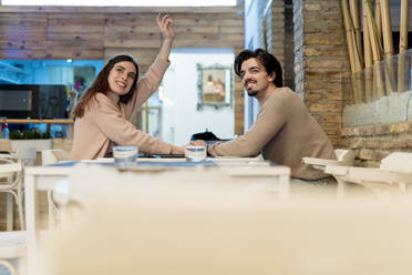 Young woman calling waiter while sitting with boyfriend at restaurant - EGAF02333