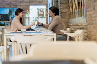 Freund und Freundin stoßen mit Wein an, während sie am Restauranttisch sitzen - EGAF02335