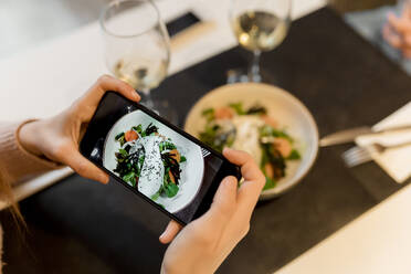 Woman photographing food through smart phone at restaurant - EGAF02341