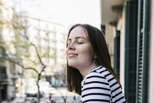 Young woman with eyes closed standing in balcony of apartment - XLGF01609