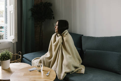 Sick woman looking away while wrapped in blanket at home - XLGF01620