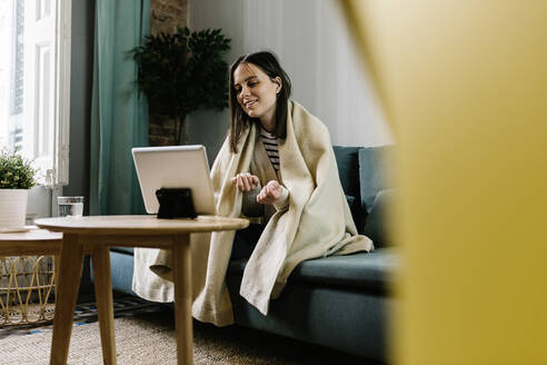 In eine Decke eingewickelte Frau spricht während eines Videoanrufs über ein digitales Tablet zu Hause - XLGF01624