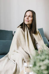 Kranke Frau, eingewickelt in eine Decke, schaut weg, während sie zu Hause sitzt - XLGF01625