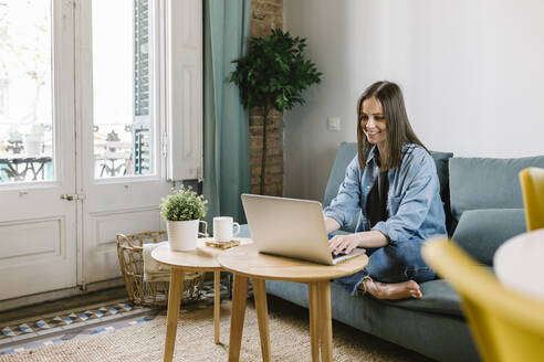 Businesswoman smiling while looking at laptop during video conference at home office - XLGF01634