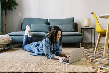 Smiling woman using laptop while lying on floor at home - XLGF01636