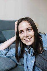 Woman looking away while leaning on sofa at home - XLGF01639