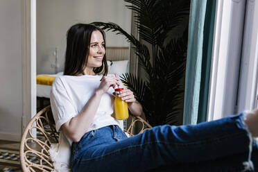 Junge Frau mit Orangensaft in der Hand, die im Wohnzimmer sitzt und nachdenkt - XLGF01642