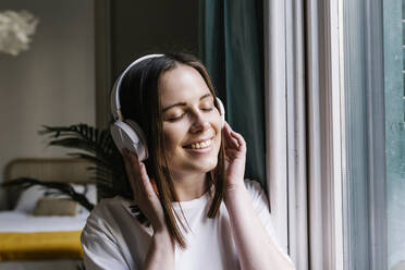 Frau lächelnd beim Hören von Musik über Kopfhörer zu Hause - XLGF01646