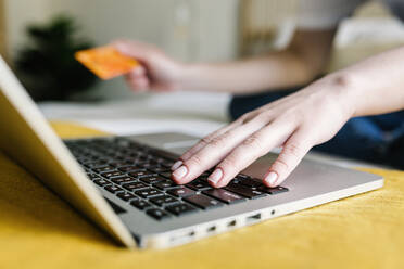 Frau beim Online-Einkauf über einen Laptop, während sie eine Kreditkarte zu Hause hält - XLGF01656