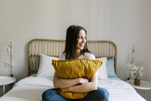 Lächelnde Frau umarmt Kissen auf dem Bett zu Hause - XLGF01659