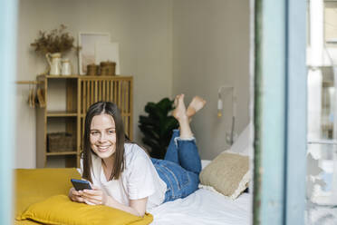 Glückliche Frau mit Mobiltelefon auf dem Bett liegend - XLGF01663