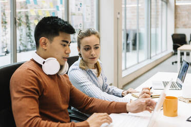 Male and female colleagues discussing over laptop at office - XLGF01677