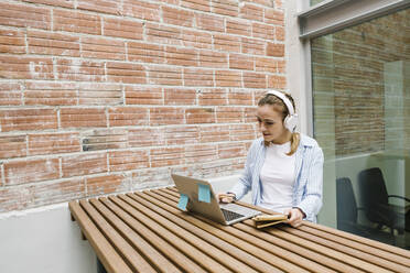 Weibliche Berufstätige mit Kopfhörern bei einem Videogespräch am Laptop in der Cafeteria - XLGF01689
