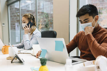 Male and female professionals wearing protective face mask while working at office - XLGF01701