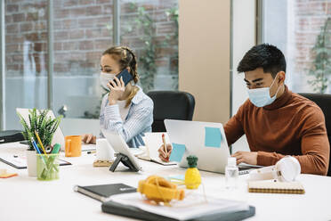 Male and female professionals using laptop at office during COVID-19 - XLGF01702