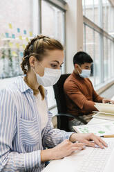 Female professional using laptop by male colleague working in coworking office during pandemic - XLGF01705