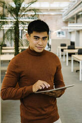 Smiling male professional with digital tablet standing in coworking office - XLGF01714