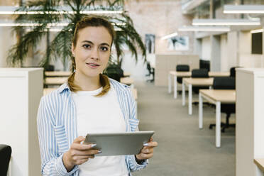 Junge Unternehmerin mit digitalem Tablet im Büro stehend - XLGF01716