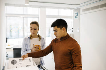 Businessman removing printout from by female colleague at office - XLGF01719