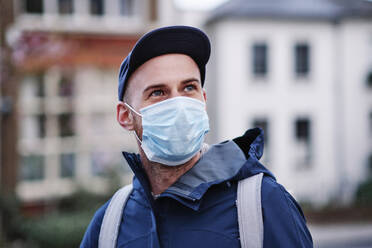 Man with gray eyes looking away while wearing protective face mask during pandemic - ASGF00252