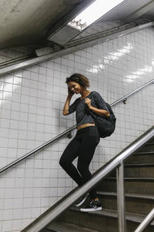 Junge Frau mit Kopf in der Hand, die auf einer Treppe in der U-Bahn nach unten geht - BOYF01975