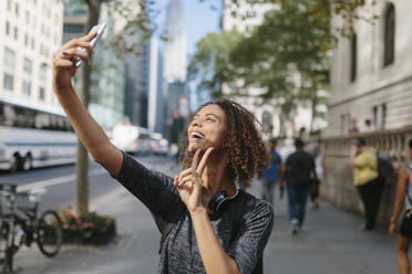 Frau zeigt Friedenszeichen, während sie ein Selfie mit dem Handy in der Stadt macht - BOYF01986