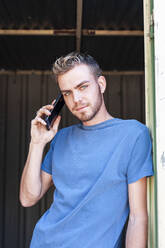 Young man talking on mobile phone while standing at doorway - JMPF00943