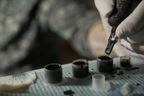 Nahaufnahme von Ernte unerkennbar Tätowierer Eintauchen Tattoo-Maschine in schwarzer Tinte bei der Arbeit im Salon - ADSF23366