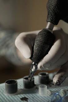 Nahaufnahme von Ernte unerkennbar Tätowierer Eintauchen Tattoo-Maschine in schwarzer Tinte bei der Arbeit im Salon - ADSF23367