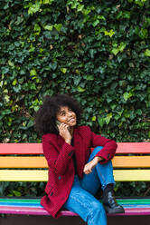 Inhalt Afroamerikanische Frau sitzt auf einer Bank in der Stadt und spricht mit ihrem Smartphone, während sie wegschaut - ADSF23374