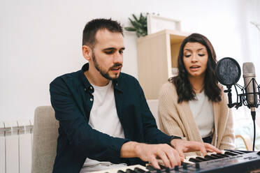 Männlicher Musiker spielt Synthesizer und singt zusammen mit einer Frau bei der Aufnahme eines Songs zu Hause - ADSF23406