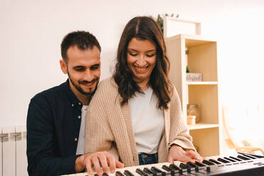 Männlicher Musiker spielt Synthesizer und singt zusammen mit einer Frau bei der Aufnahme eines Songs zu Hause - ADSF23408