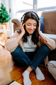 Fröhliche Musikerin, die ein Lied über Kopfhörer hört, während sie zu Hause Musik komponiert - ADSF23422