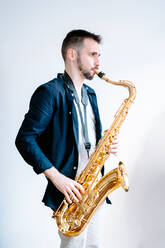 Seitenansicht eines kreativen männlichen Musikers, der Saxophon spielt, während er auf einem weißen Hintergrund steht und wegschaut - ADSF23424