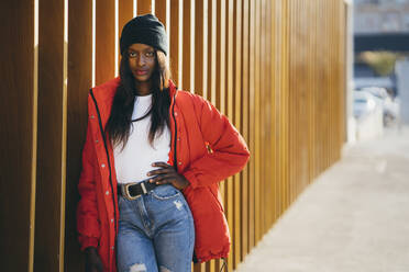 Beautiful woman with hand on hip leaning on wooden wall - MPPF01699