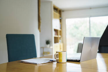 Laptop mit Kaffeetasse und Buch auf dem Tisch zu Hause - AFVF08694