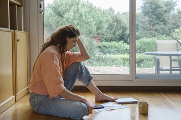 Woman with head in hands looking at bills and receipts while sitting at home - AFVF08696