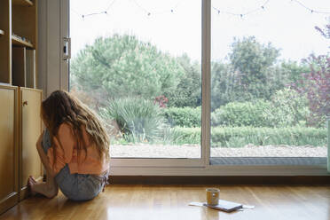 Sad woman with long hair sitting while hugging knees at home - AFVF08699