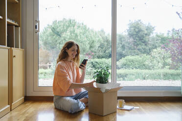 Woman photographing plant through smart phone while sitting at home - AFVF08705