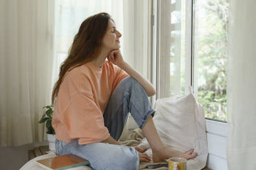 Woman with hand on chin sitting on mattress at home - AFVF08711