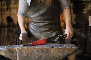 Schmied macht Messer aus Metall auf Amboss in Schmiede - AODF00474