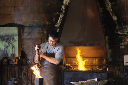 Junger männlicher Schmied verbrennt Metall im Feuer in der Werkstatt - AODF00477