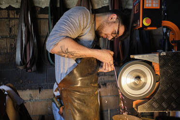 Craftsman sharpening metal on grinder at workshop - AODF00482