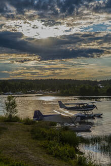 Finnland, Lappland, Inari, Dramatischer Sonnenuntergang über Wasserflugzeugen, die am Ufer des Inari-Sees liegen - RUNF04348