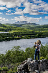 Mutter bewundert die Aussicht auf den Fluss Karasjohka mit ihrem kleinen Sohn in den Händen - RUNF04355