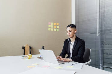 Businesswoman with in-ear headphones using laptop at office - MEUF02532