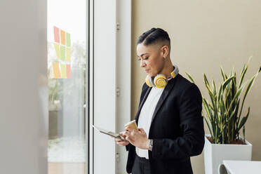 Junge Geschäftsfrau mit Kaffeetasse und digitalem Tablet im Büro - MEUF02571
