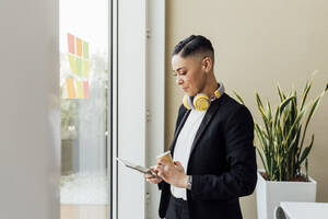 Young businesswoman with coffee cup using digital tablet in office - MEUF02571